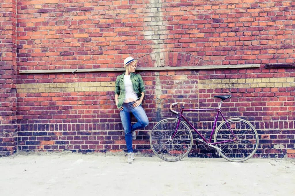 A person leaning against a brick wall with a bicycle.