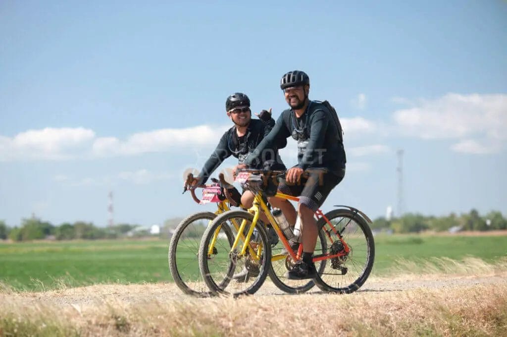 Two men riding bikes on a dirt road.
