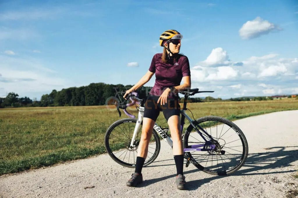 A woman is posing with her bike on a dirt road.