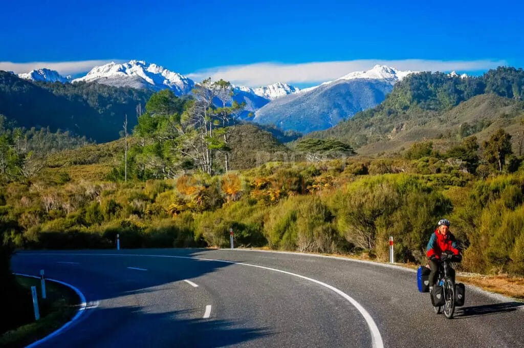 A cyclist rides down a road with mountains in the background.