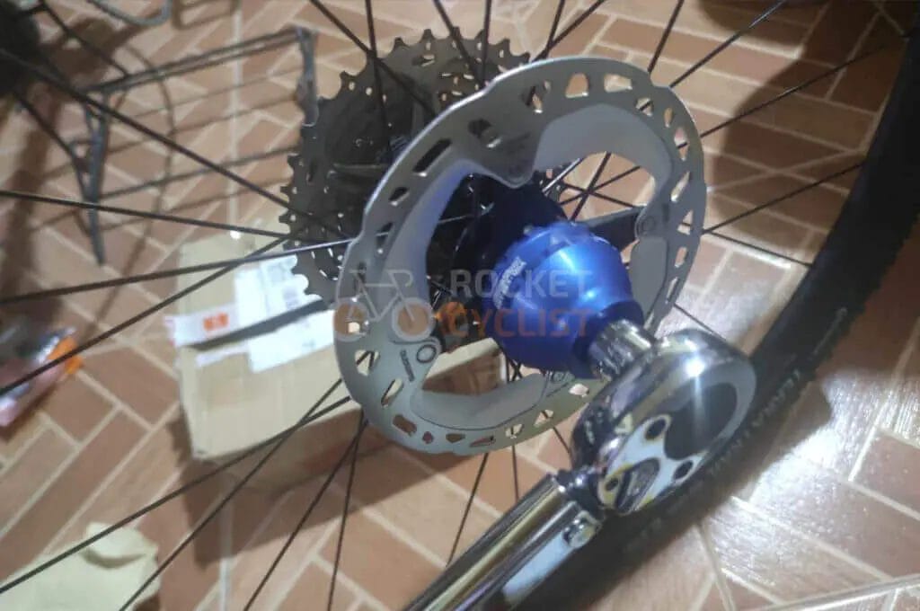 Close-up of a bicycle wheel hub and disc brake rotor with a partial view of a crank arm.