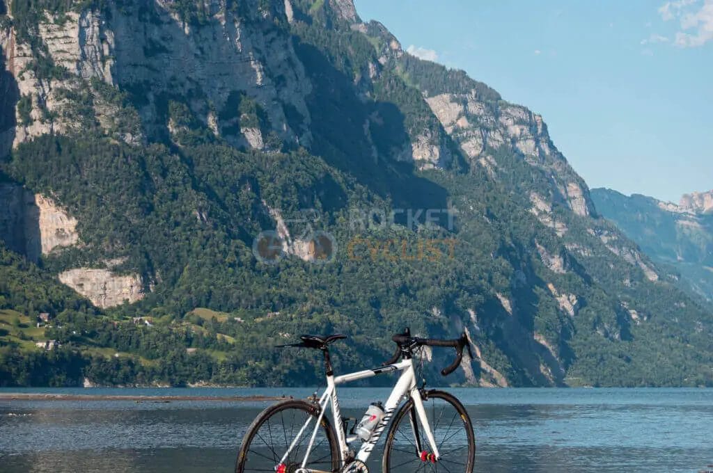 A bicycle is parked near a lake with mountains in the background.
