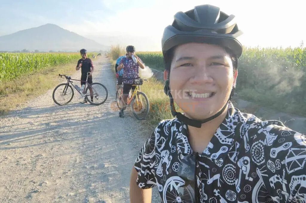 A man on a bicycle taking a selfie on a dirt road.