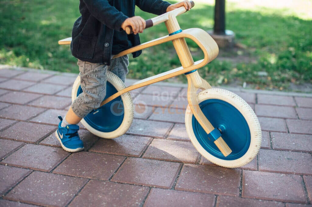 A young boy riding a wooden bike in a park.