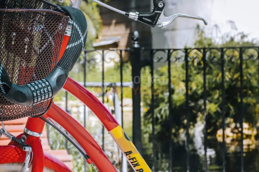 A red bicycle is parked next to a fence.