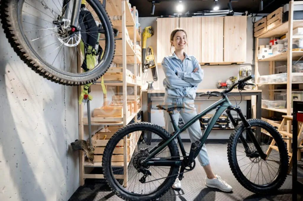 A woman standing in a garage with a mountain bike.