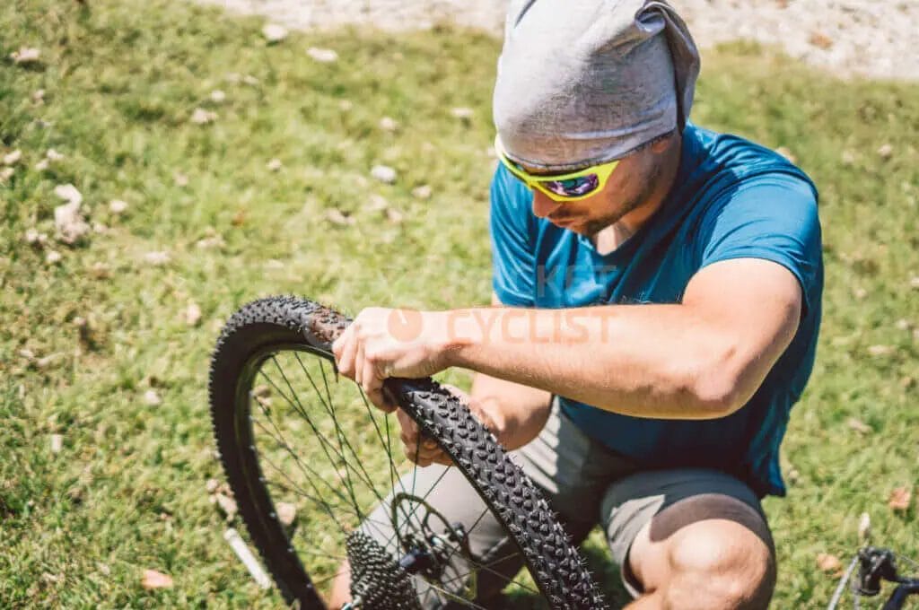 A man fixing a bicycle tire in the grass.