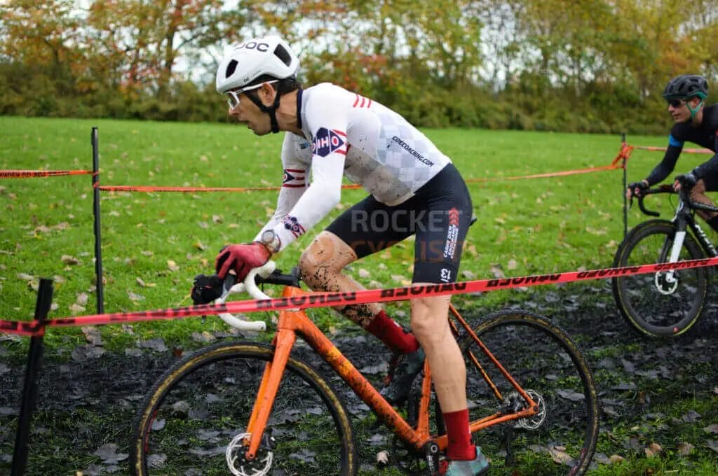 Two cyclists racing in a muddy field.