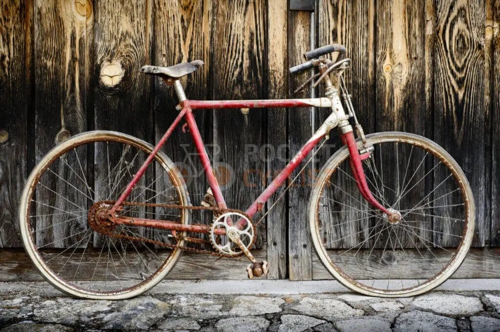 An old rusty bicycle leaning against a wooden door.