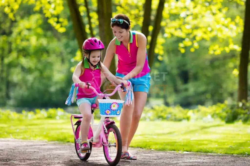 A woman teaching a girl to ride a bike.