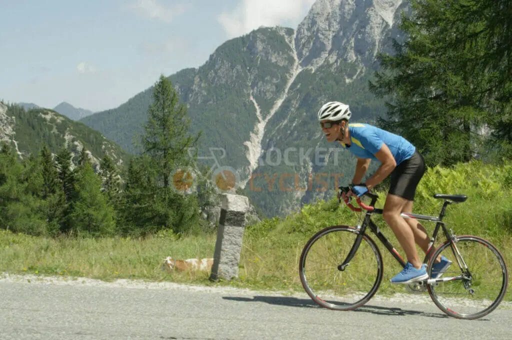 A cyclist riding down a road with mountains in the background.