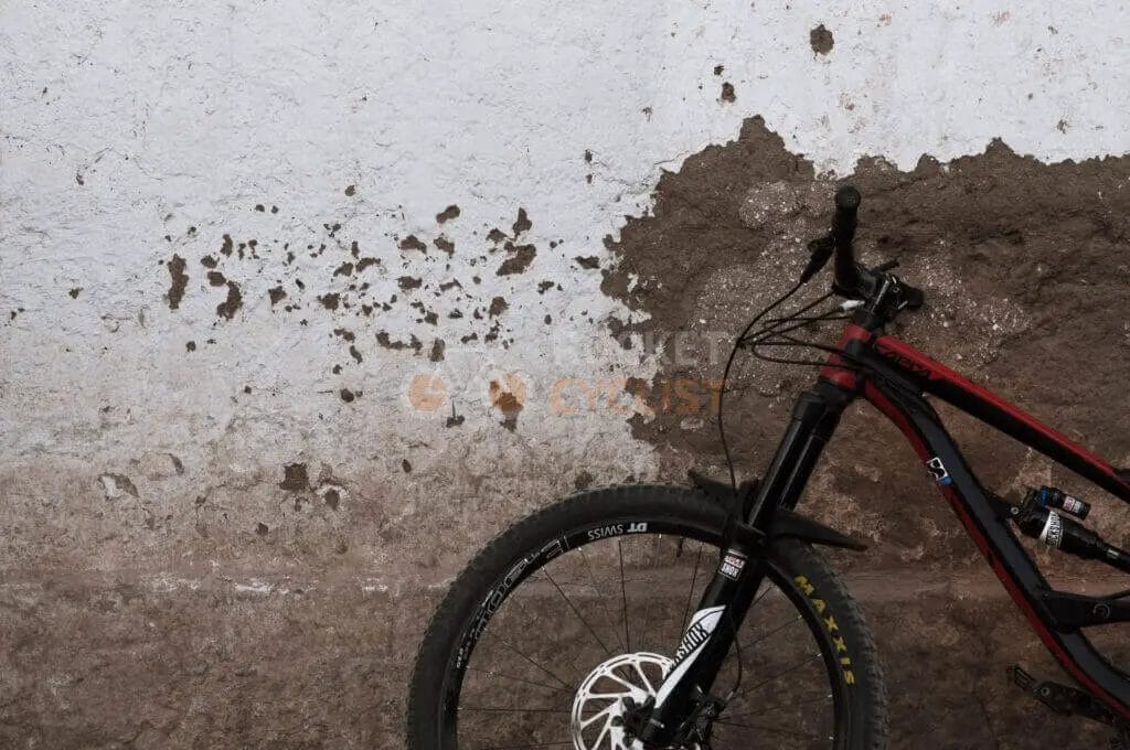 A partial view of a mountain bike against a deteriorating wall with peeling paint.