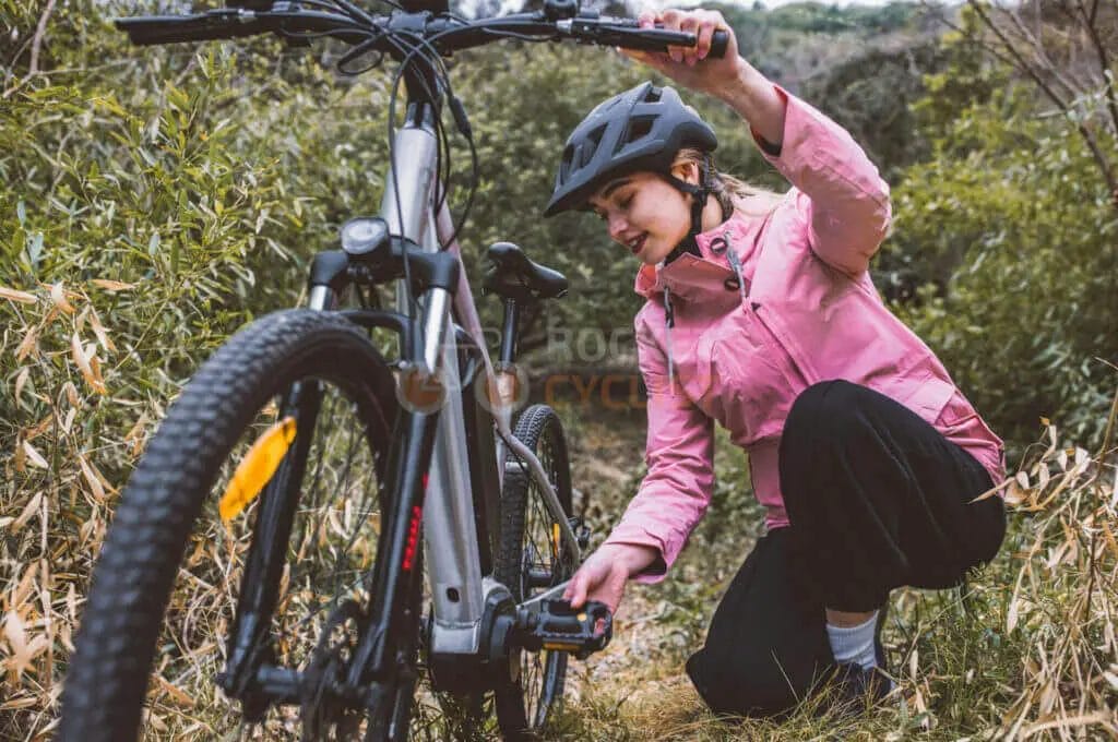 A woman fixing her bicycle in the woods.
