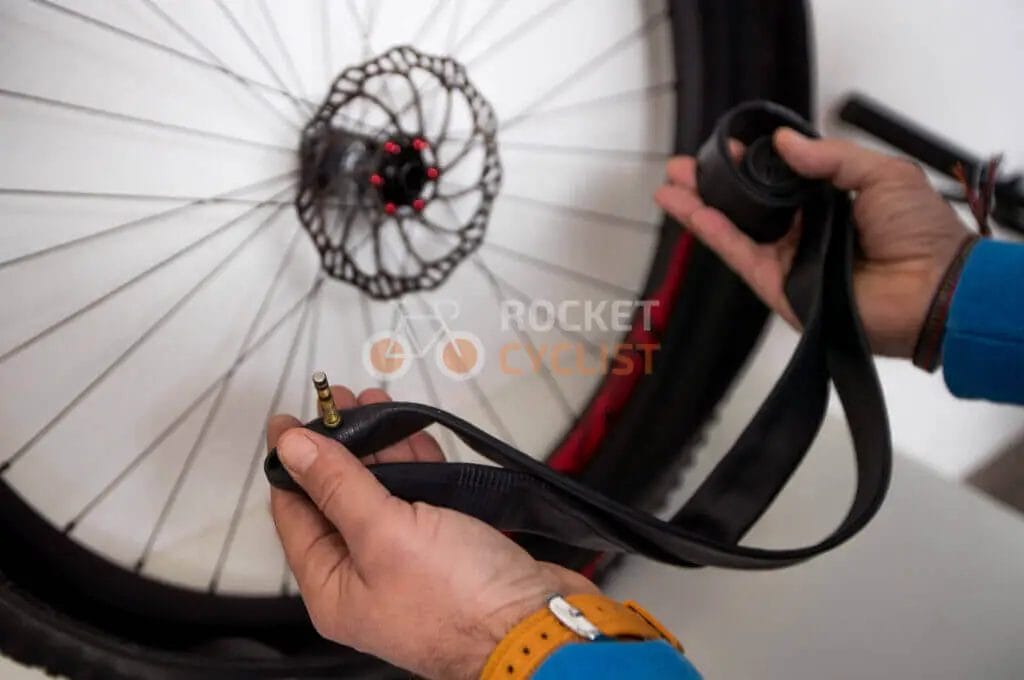 Person holding a bicycle inner tube and tire lever with a bike wheel in the background.