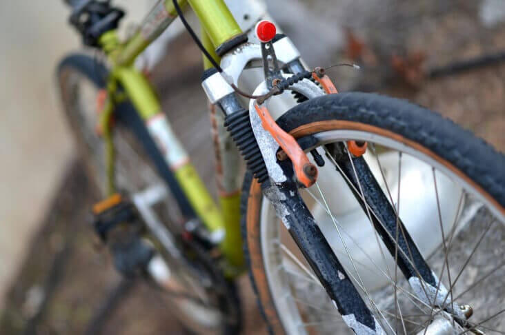 Close-up of the front suspension fork and wheel of a green mountain bike with visible signs of wear and dirt on the tire and fork.