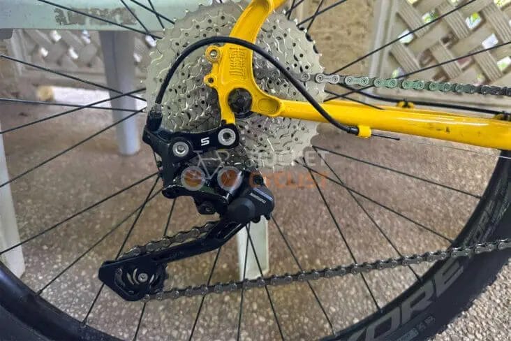 Close-up view of a yellow bicycle's rear derailleur and cassette gears, featuring a Bicycle Goatlink for improved efficiency and smoother shifting.